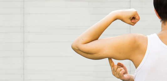 woman flexing bicep while pointing to her arm to detect muscle loss
